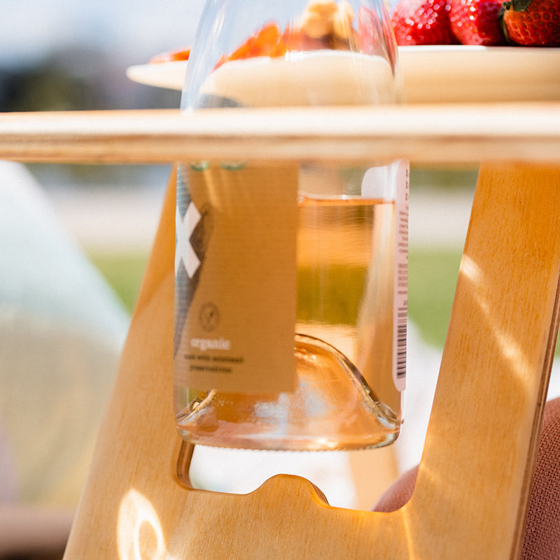 A close up of a rose wine bottle being placed into the wine bottle anchor on the Outdoors Hello folding picnic table.
