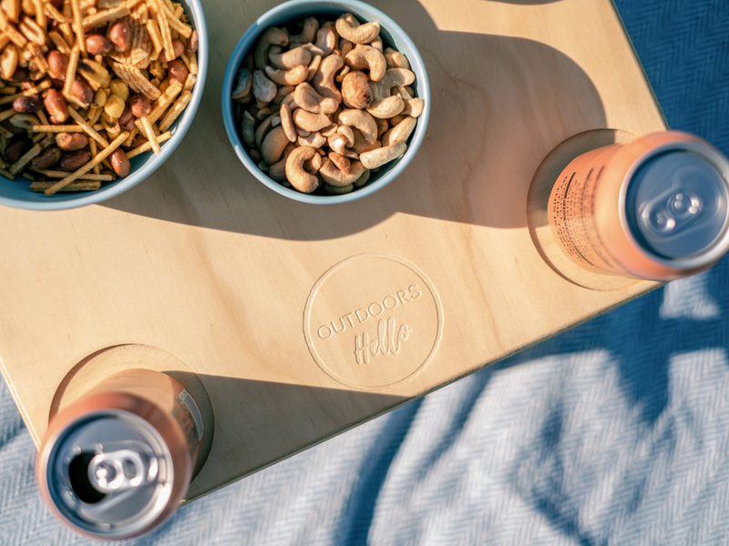 Outdoors Hello logo close up on a Divine Folding Picnic Table with cashews and snack mix