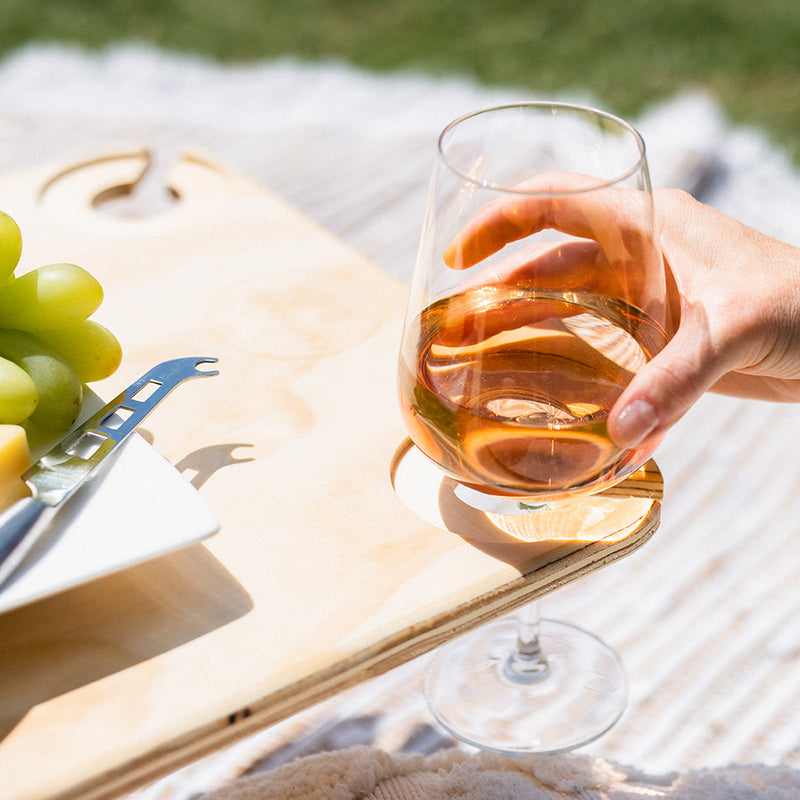 A glass full of rose wine being placed into the wine glass slot on the Outdoors Hello folding picnic table.