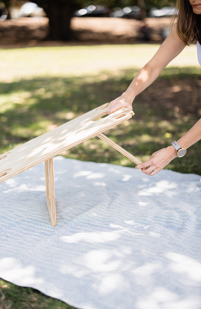 Woman's hands unfolding the second leg on a folded picnic table onto a picnic rug.