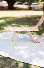 Woman's hands placed on the leg and table top of a folding picnic table on a picnic rug.
