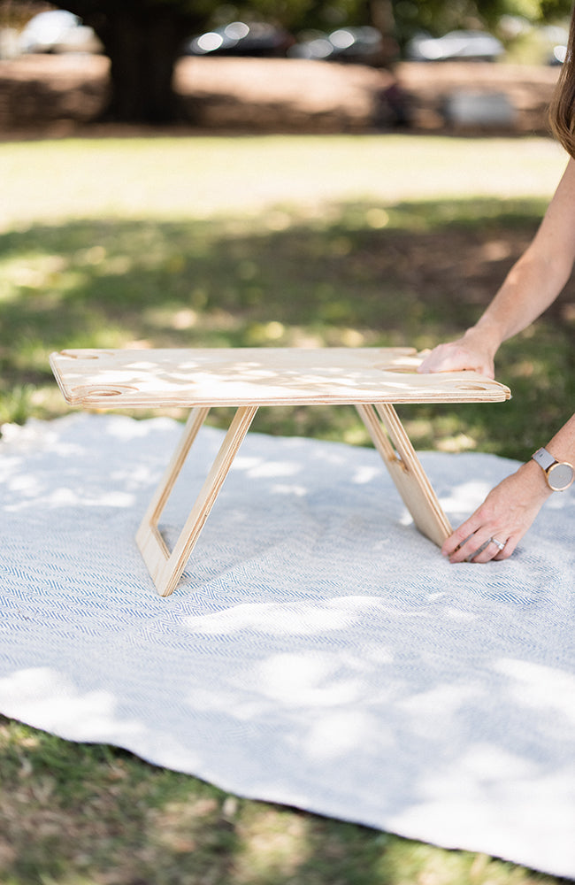 Woman's hands placed on the leg and table top of a folding picnic table on a picnic rug.
