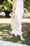 Woman in white maxi skirt carrying a folding picnic table in the park walking towards a picnic rug.